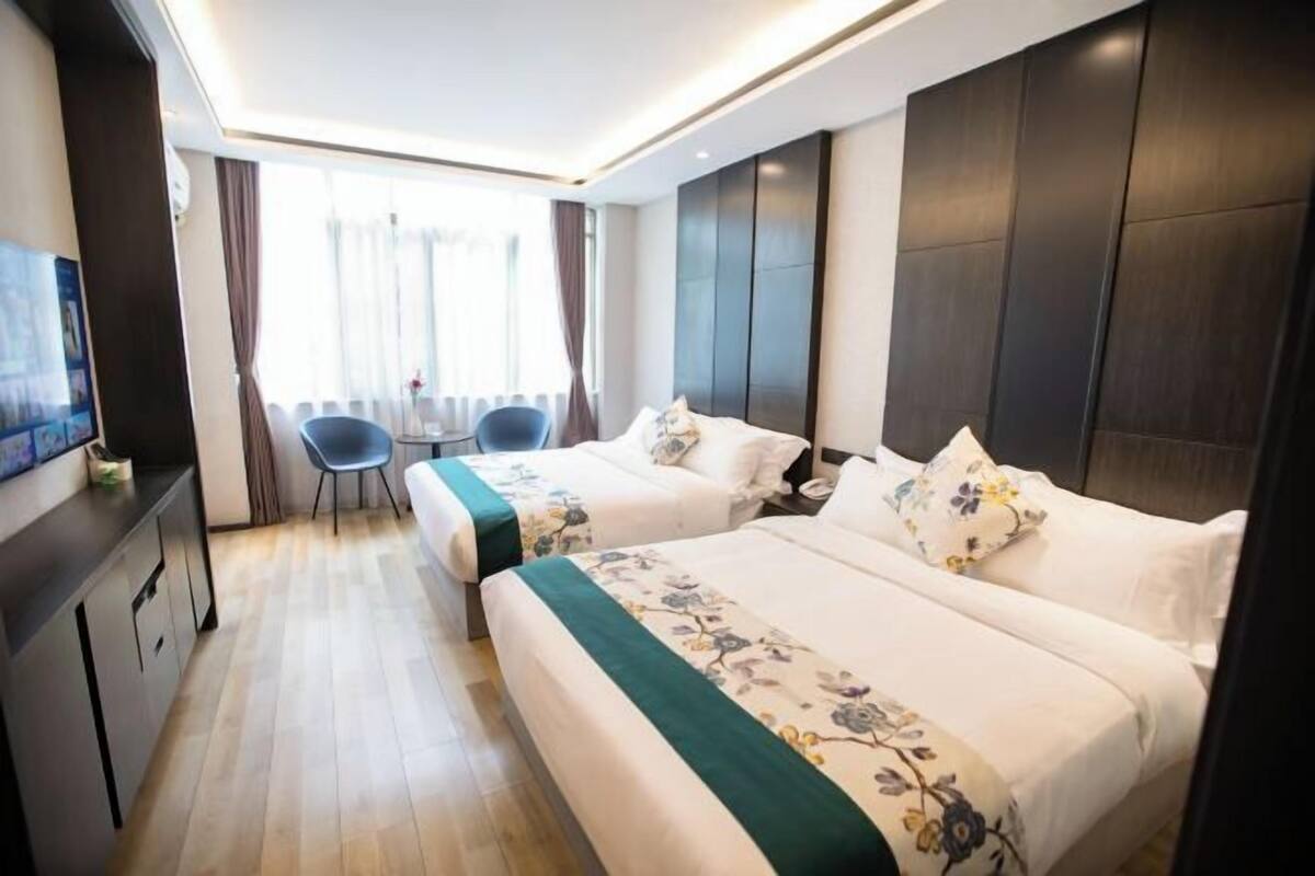 A hotel room with two beds, a desk, a chair, and a television.