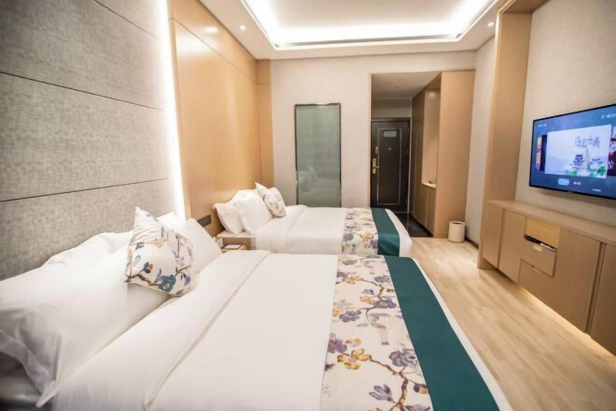 A hotel room with two beds, a TV, a wooden floor, and a modern design.