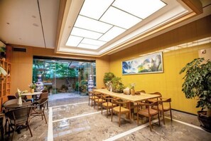 A hotel lobby with a dining area, a large painting on the wall, and a view of the outdoors. - Hongting Garden Hotel (Kunming)