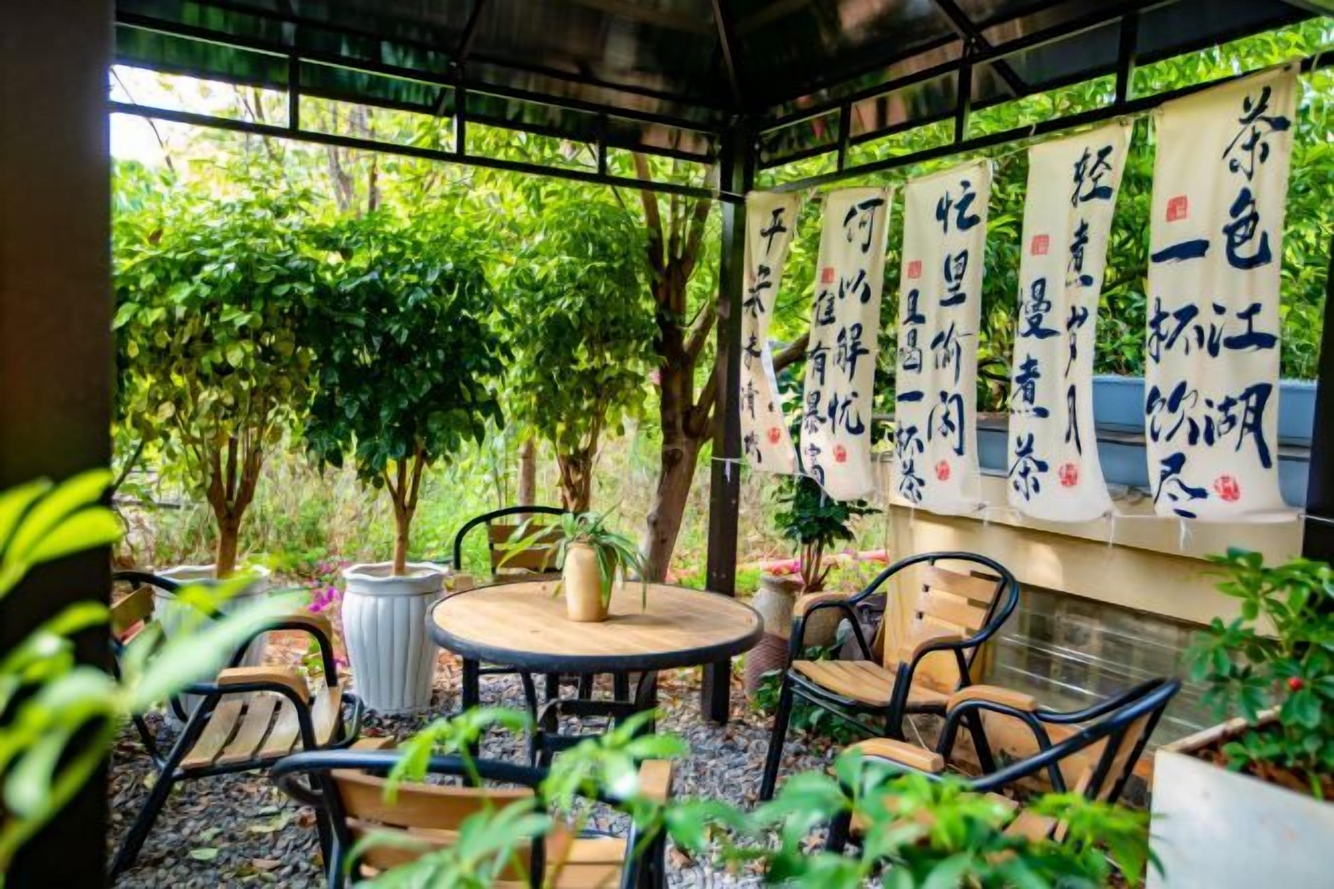 An outdoor seating area with tables and chairs, surrounded by greenery and traditional Chinese calligraphy banners.