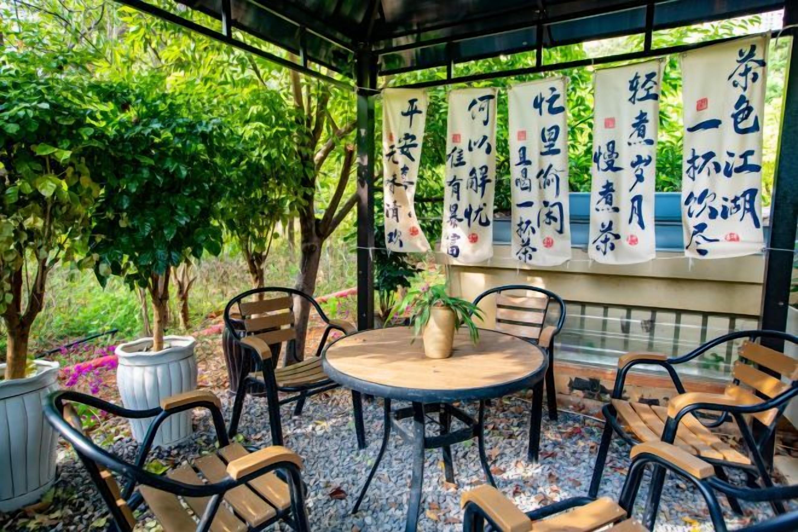 An outdoor seating area with round tables and chairs, surrounded by potted plants and trees.