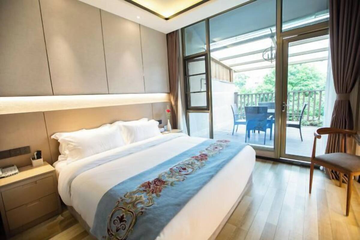 A hotel room with a large bed, a nightstand, a chair, and a balcony with outdoor furniture.