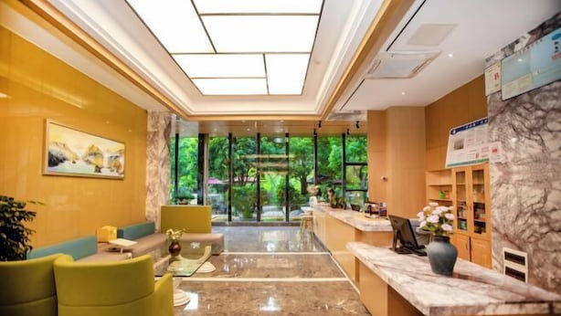 A hotel reception area with a marble floor, a reception desk, seating area, and a view of greenery through large windows. - Hongting Garden Hotel (Kunming)