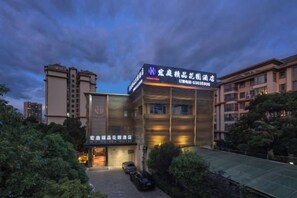 A hotel with a modern facade, signage indicating it is a hotel, and a parking area in front. - Hongting Garden Hotel (Kunming)