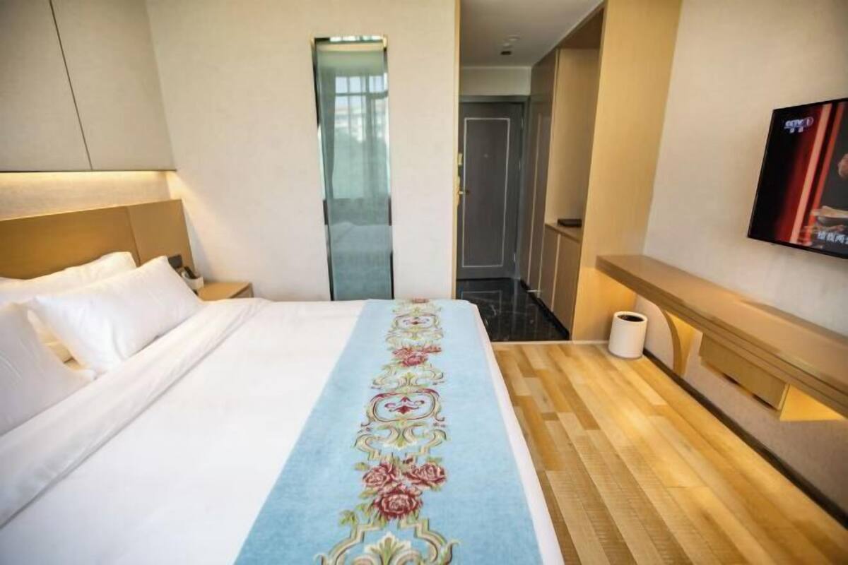 A hotel room with a bed, a television, a bathroom, and a hallway.