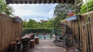 A wooden deck with a swing chair, potted plants, and a view of a garden. - Hongting Garden Hotel (Kunming)