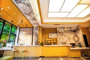 A modern reception area with a marble accent wall, a reception desk, and a large window providing a view of greenery. - Hongting Garden Hotel (Kunming)