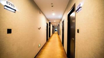 A hotel hallway with a carpeted floor, doors on both sides, and illuminated signs indicating room numbers.