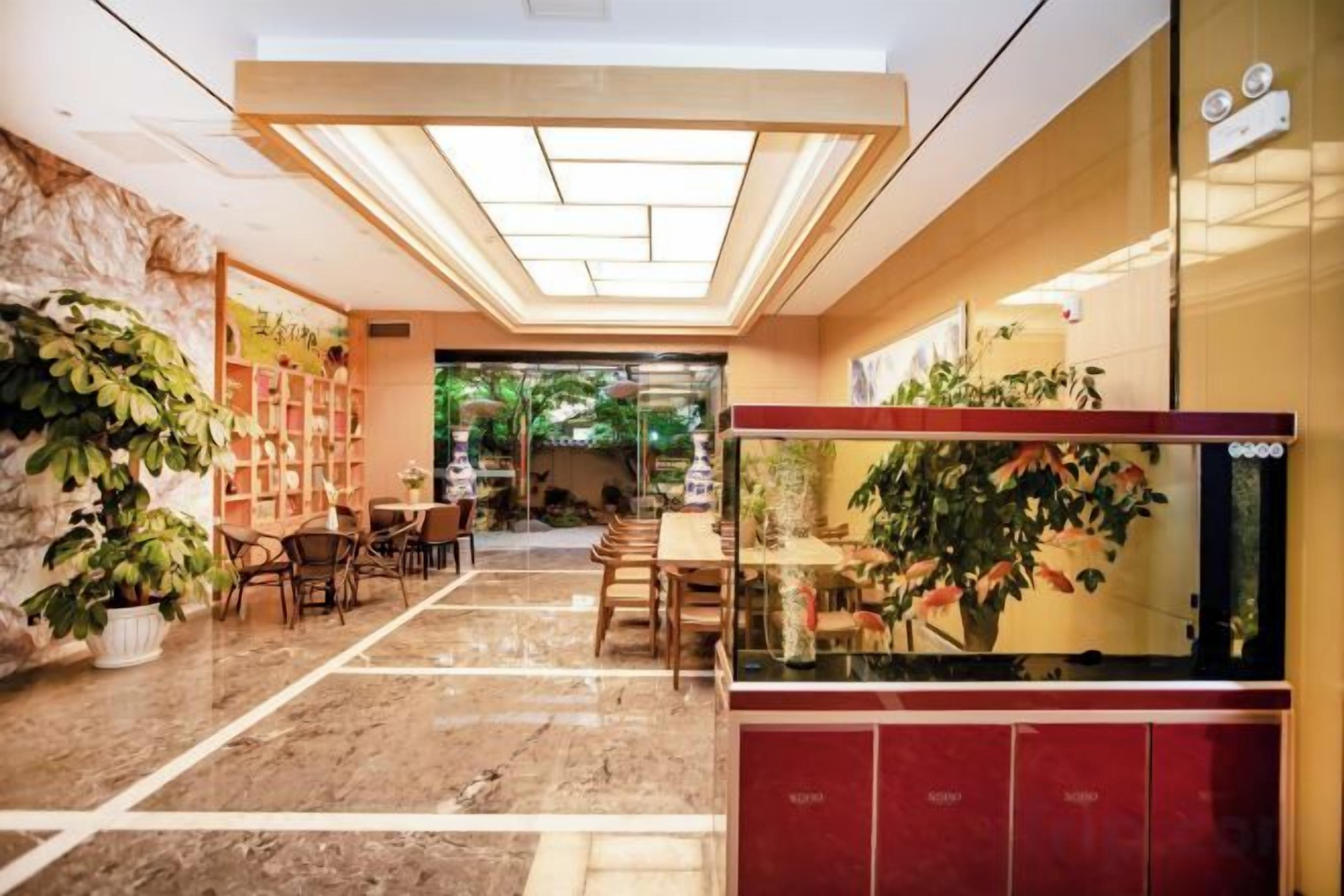 En hotellobby med et marmorgulv, en receptionsdisk, et akvarium og et siddeområde med stole og borde.