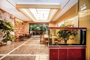 Un hall de hotel con piso de mármol, un mostrador de recepción, un acuario y una zona de estar con sillas y mesas.