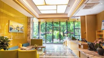 Vestíbulo de hotel con mostrador de recepción, zona de estar y grandes ventanales con vistas a zonas verdes.
