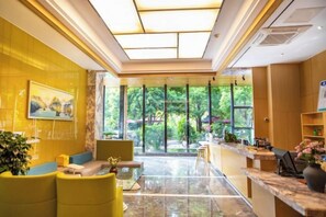 A hotel lobby with a reception desk, seating area, and large windows offering a view of greenery. - Hongting Garden Hotel (Kunming)