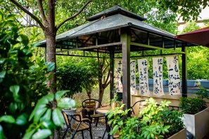 A covered outdoor seating area with tables and chairs, surrounded by greenery and a pergola structure. - Hongting Garden Hotel (Kunming)