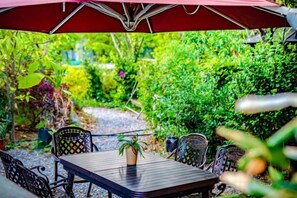 Un patio al aire libre con una mesa y sillas, rodeado de abundante vegetación.