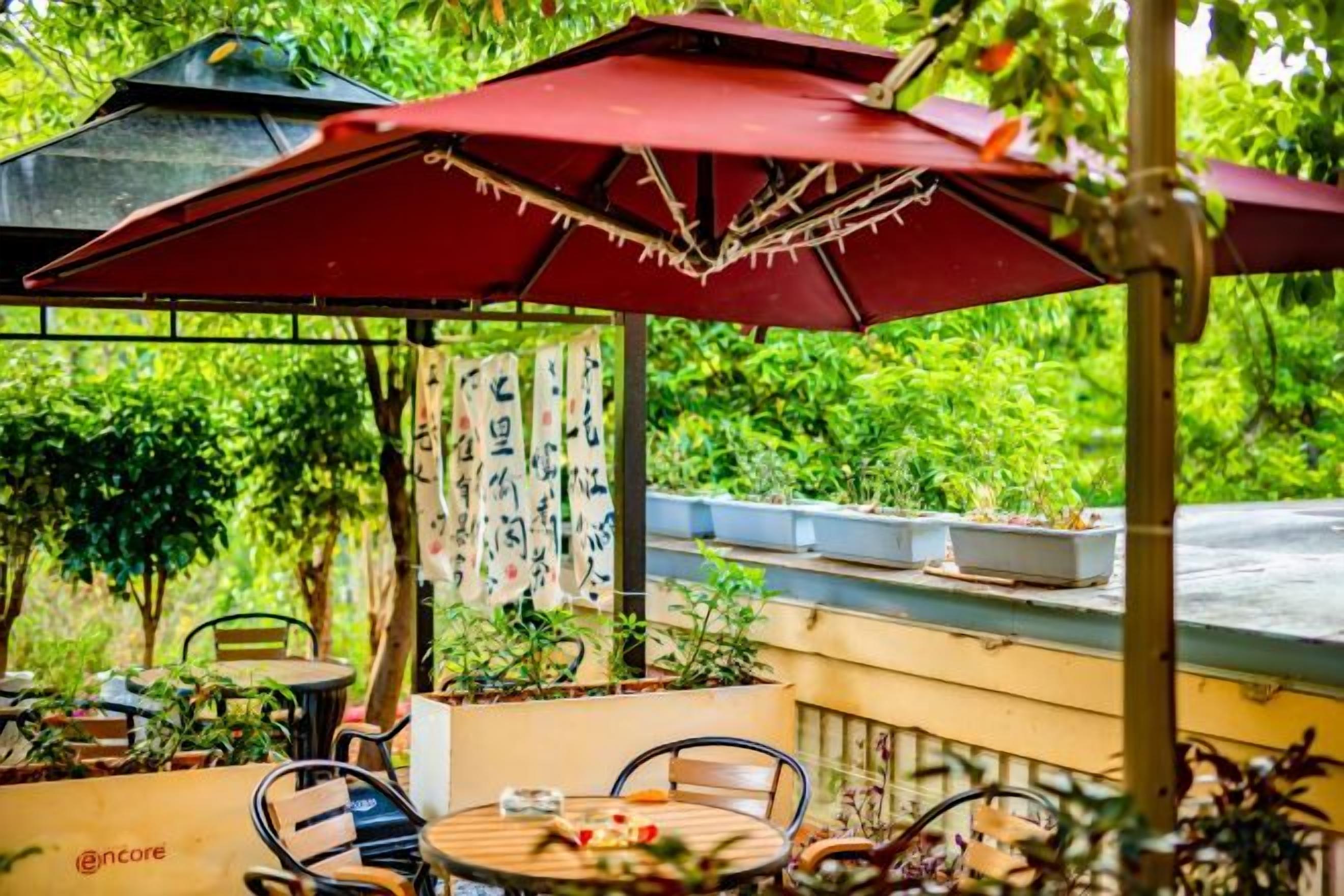 Una terrazza esterna con un ombrello rosso, un tavolo rotondo e delle sedie.