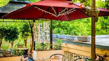 Una terrazza esterna con un ombrello rosso, un tavolo rotondo e delle sedie.