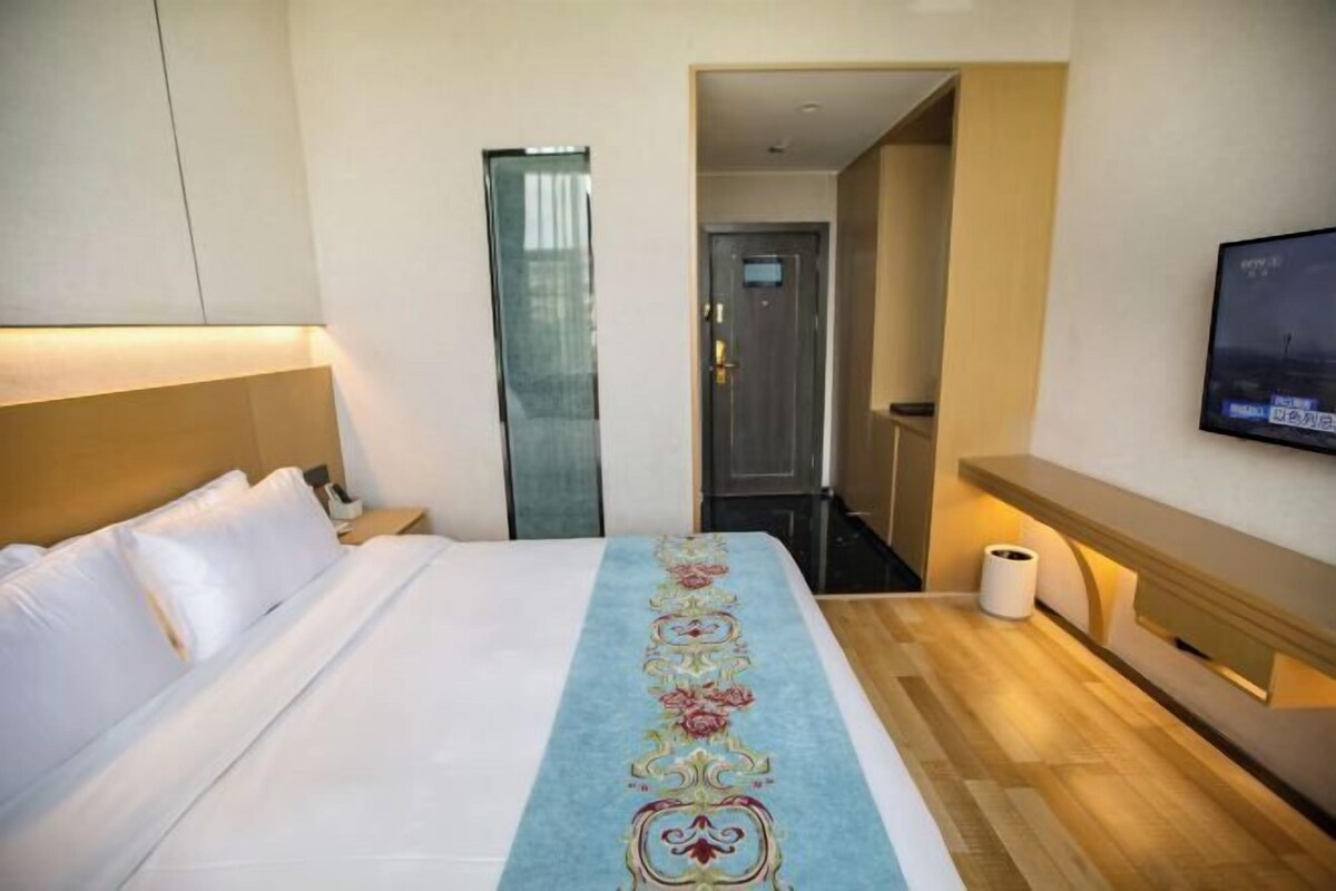 Ett hotellrum med en säng, en tv på väggen och en hall som leder till ett annat rum.