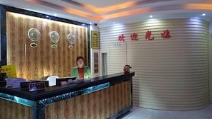 A reception desk with a patterned backdrop, a receptionist, and a wall with red text. - Shanghai Xinyao Hotel (Minhang Jiangchuan Road Subway Station Branch) (Shanghai)