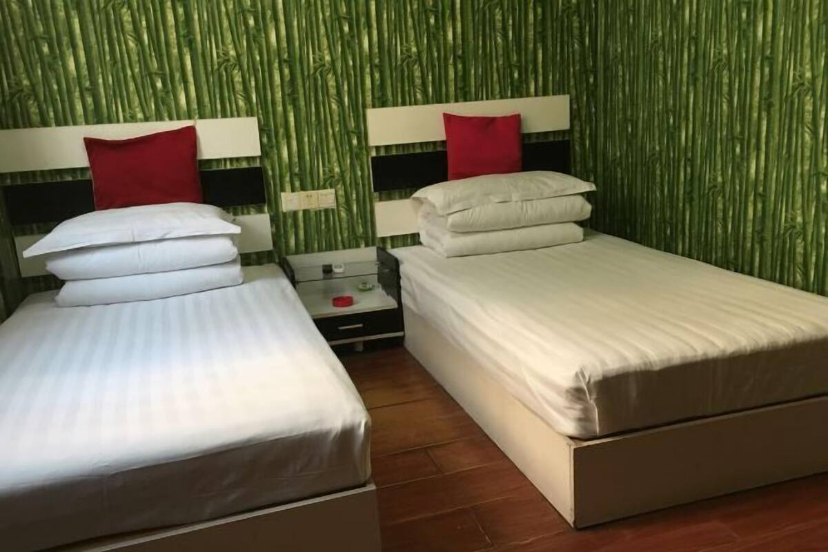 Habitación con dos camas, cada una con ropa de cama blanca y almohadas rojas, frente a una pared con diseño de bambú verde.