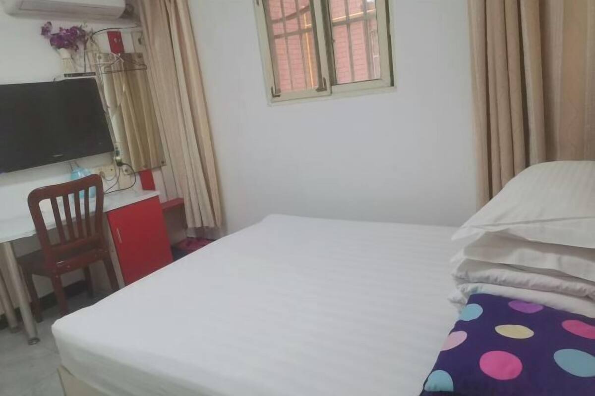 Un dormitorio con cama, escritorio y silla, televisor y ventana con cortinas.