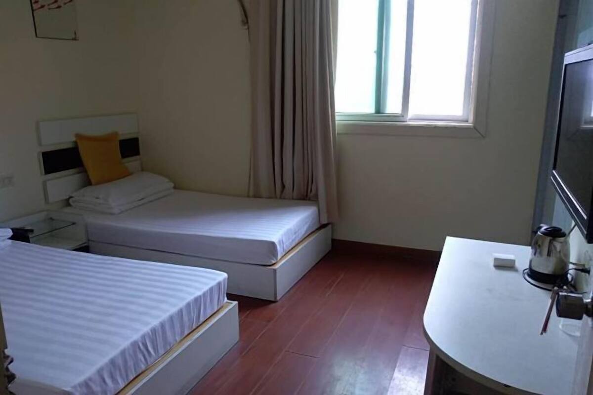 Habitación de hotel con dos camas individuales, una mesita con una tetera y una ventana con cortinas.