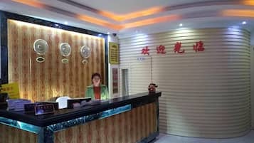 Uma área de recepção com um balcão curvo, um recepcionista e uma parede com caracteres chineses.