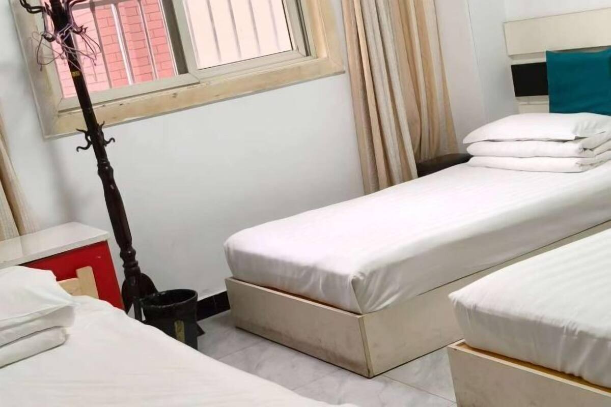 Una habitación pequeña y limpia con dos camas individuales, una ventana con cortinas y una mesita de noche.