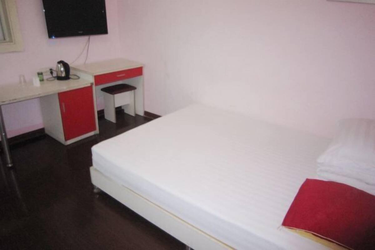Un dormitorio con una cama, un escritorio, una silla y un televisor en la pared.