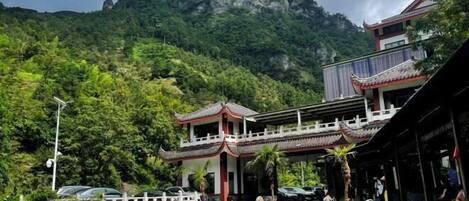 A traditional building with a swimming pool, surrounded by lush greenery and a mountain backdrop.