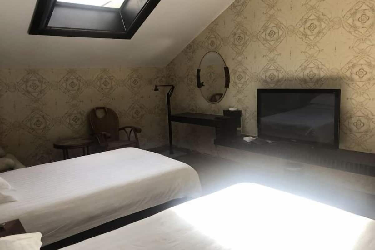 Una habitación con dos camas, un escritorio, una silla, un televisor y un tragaluz.