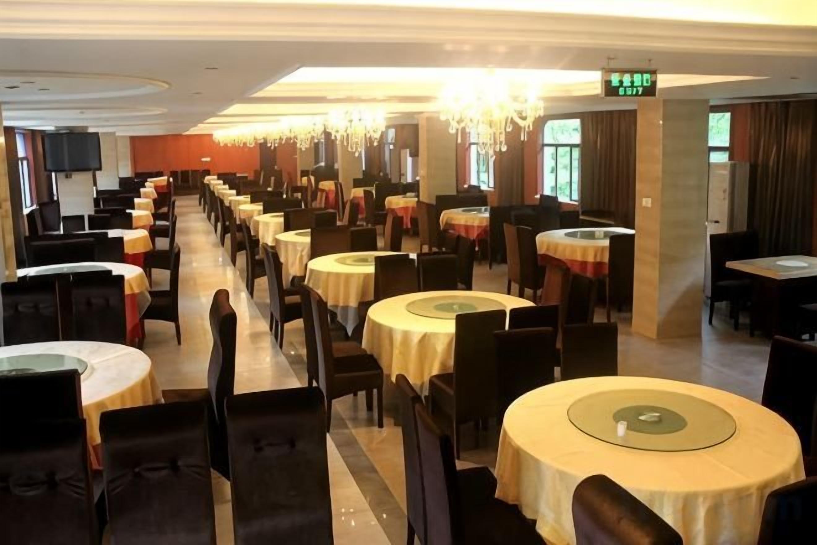 A hotel dining area with multiple round tables and chairs, a chandelier, and a television mounted on the wall.