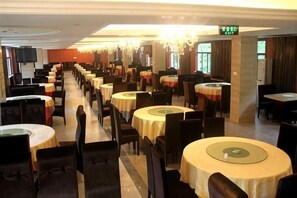Une salle à manger d’hôtel avec plusieurs tables rondes et des chaises, un lustre et un téléviseur fixé au mur.