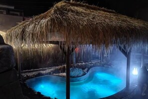 A hot tub with a thatched roof, surrounded by a stone structure, and illuminated by ambient lighting. - Hangzhou Shimenxia Hotel Resort (Hangzhou)