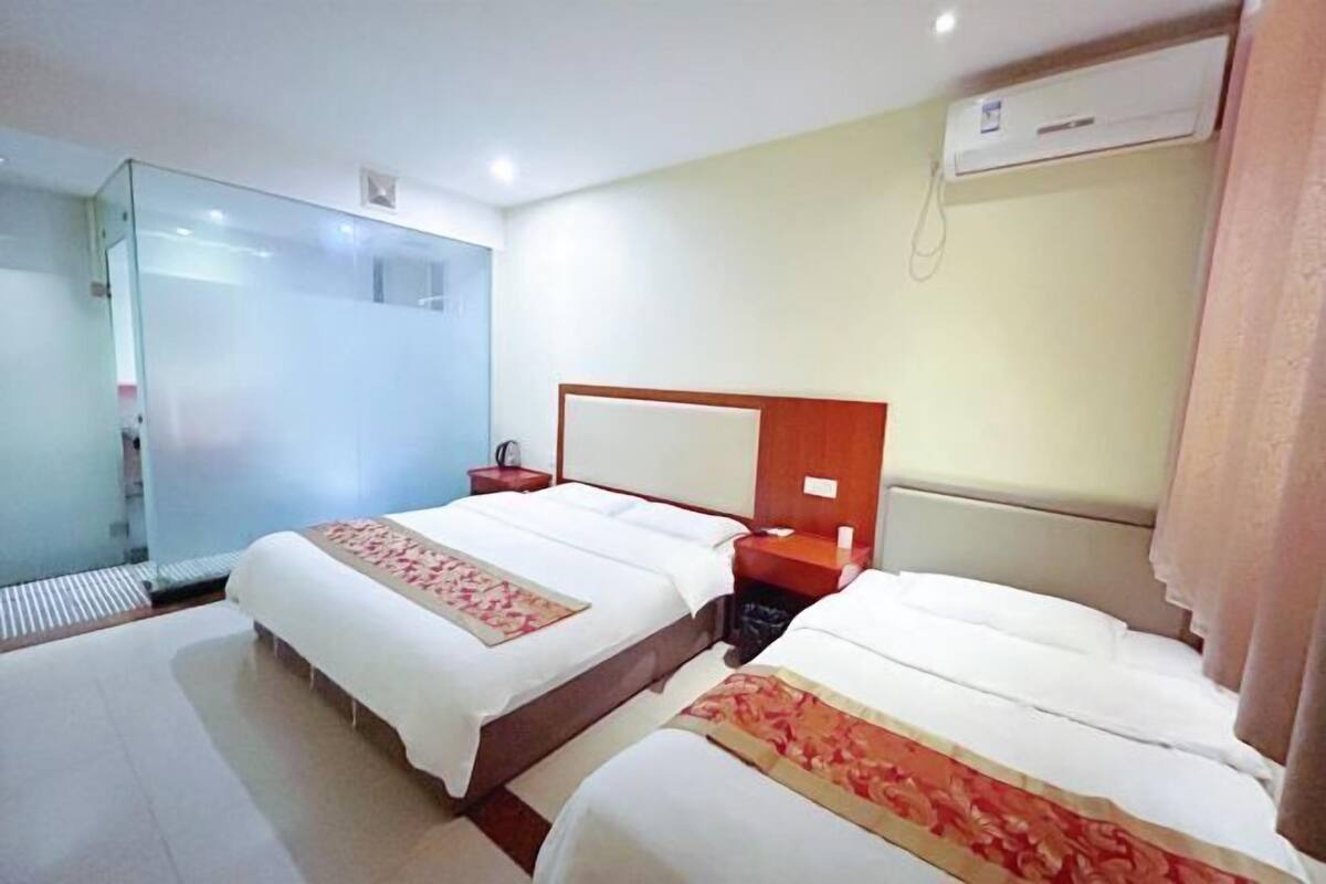 Hotellihuone, jossa on kaksi sänkyä, lasiseinä, puinen pääty ja ilmastointilaite.