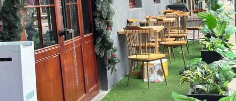 A courtyard with wooden tables and chairs, a small garden area with artificial grass, and potted plants.