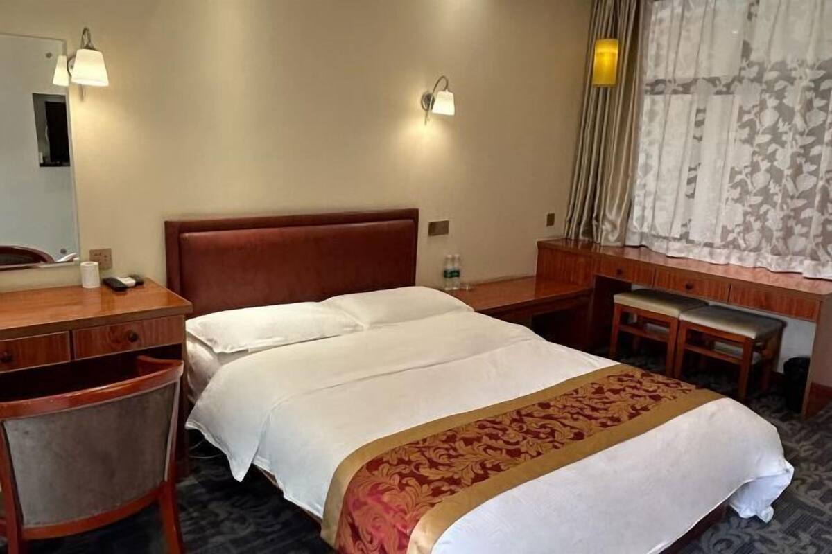Hotellihuone, jossa on sänky, työpöytä, tuoli, peili ja ikkuna, jossa on verhot.