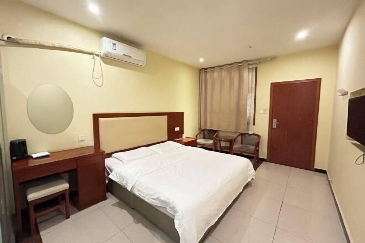 Hotellihuone, jossa on sänky, työpöytä, tuoli ja ilmastointilaite.