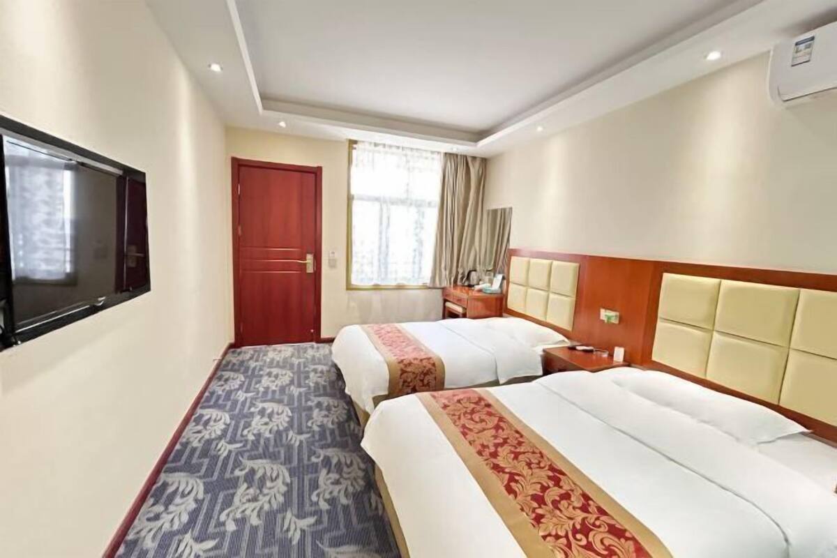 Hotellihuone, jossa on kaksi sänkyä, televisio, ikkuna verhoilla, yöpöytä ja sängynpääty.