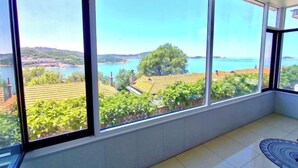 A room with large windows offering a view of a body of water, greenery, and distant buildings. - Weihai Shanhai Boutique Homestay (Weihai)