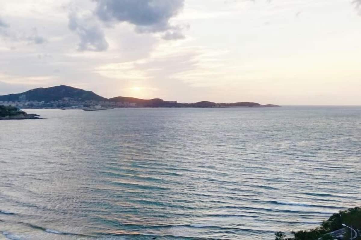 A coastal view with a calm sea, distant hills, and a clear sky.