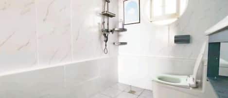 A bathroom with a bathtub, a toilet, a shower, and a small window.