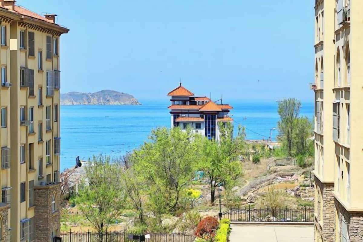A coastal building with a red roof, surrounded by greenery and overlooking the sea.