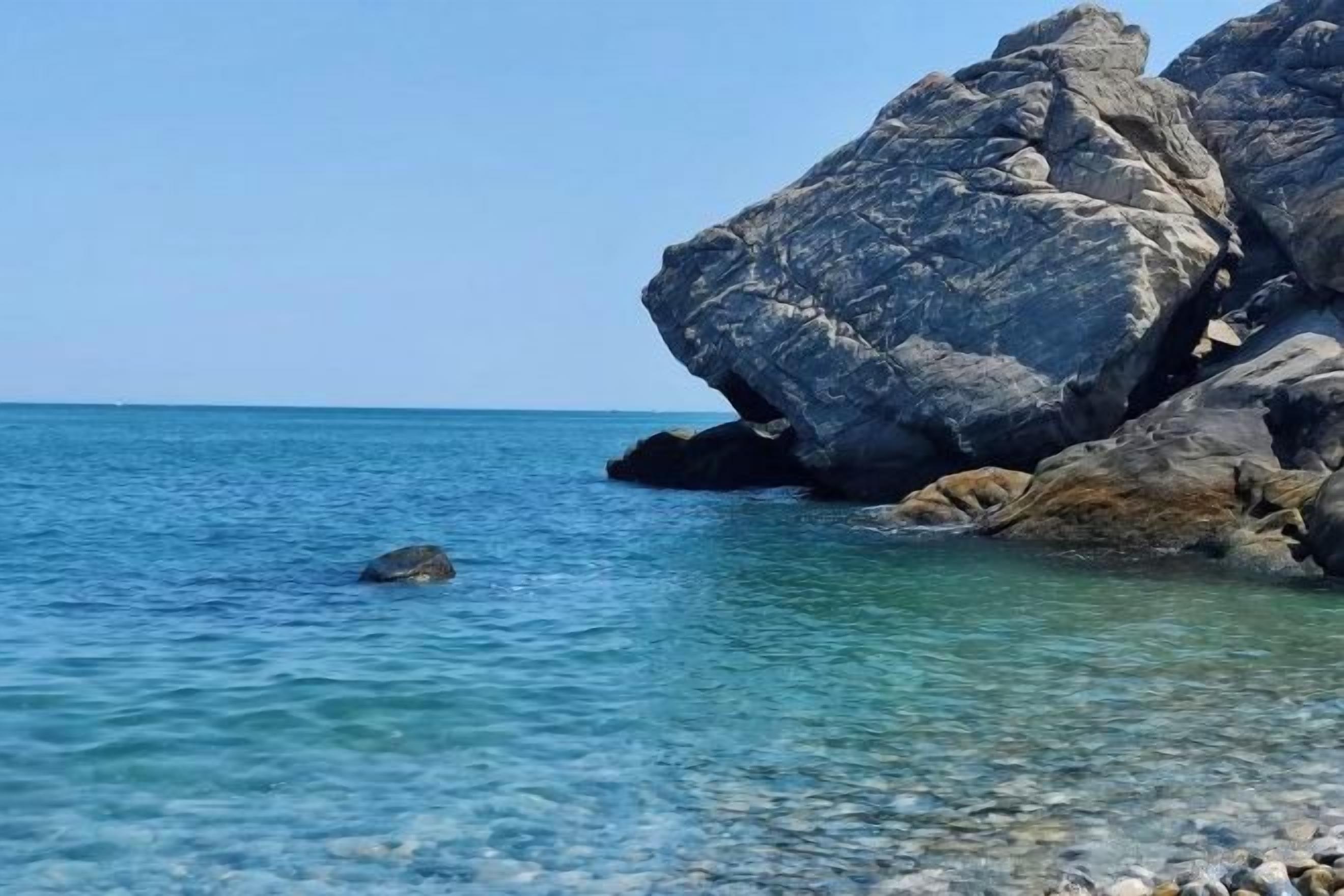 Costa rochosa com água azul límpida e uma grande formação rochosa.