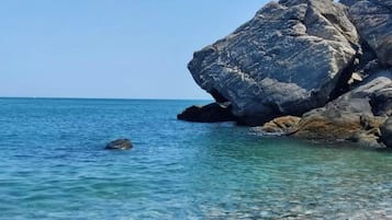 Costa rochosa com água azul límpida e uma grande formação rochosa.