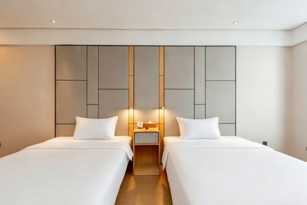 A hotel room with two beds, a modern headboard, bedside lamps, and a small table.