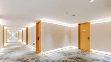 A hotel corridor with doors on both sides, carpeted floor, and recessed lighting.
