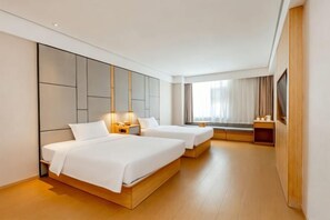 Ein Hotelzimmer mit zwei Betten, einem großen Fenster mit Vorhängen, einem Flachbildfernseher und Holzboden.