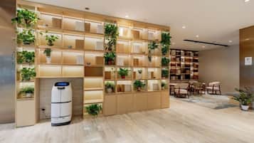 A hotel lobby with a large shelving unit displaying potted plants, a seating area with chairs, and a white cylindrical object on the floor.