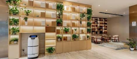 A hotel lobby with a large shelving unit displaying potted plants, a seating area with chairs, and a white cylindrical object on the floor.
