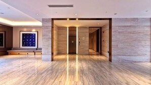 Un hall d’entrée spacieux avec un sol en marbre, une œuvre d’art encadrée au mur et un ascenseur moderne.